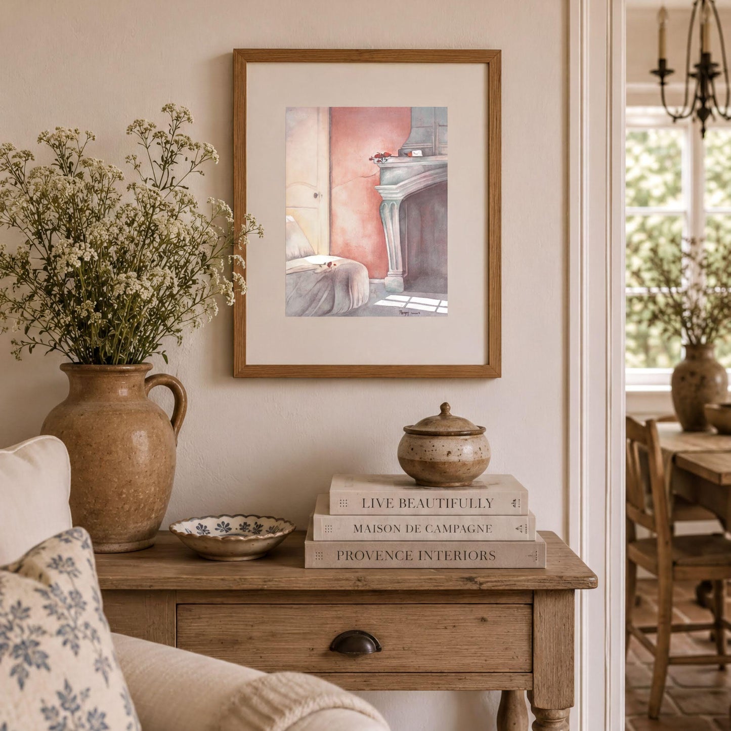 a cozy living room with a wooden table, a vase of flowers, a framed painting of a room, and a stack of books.
