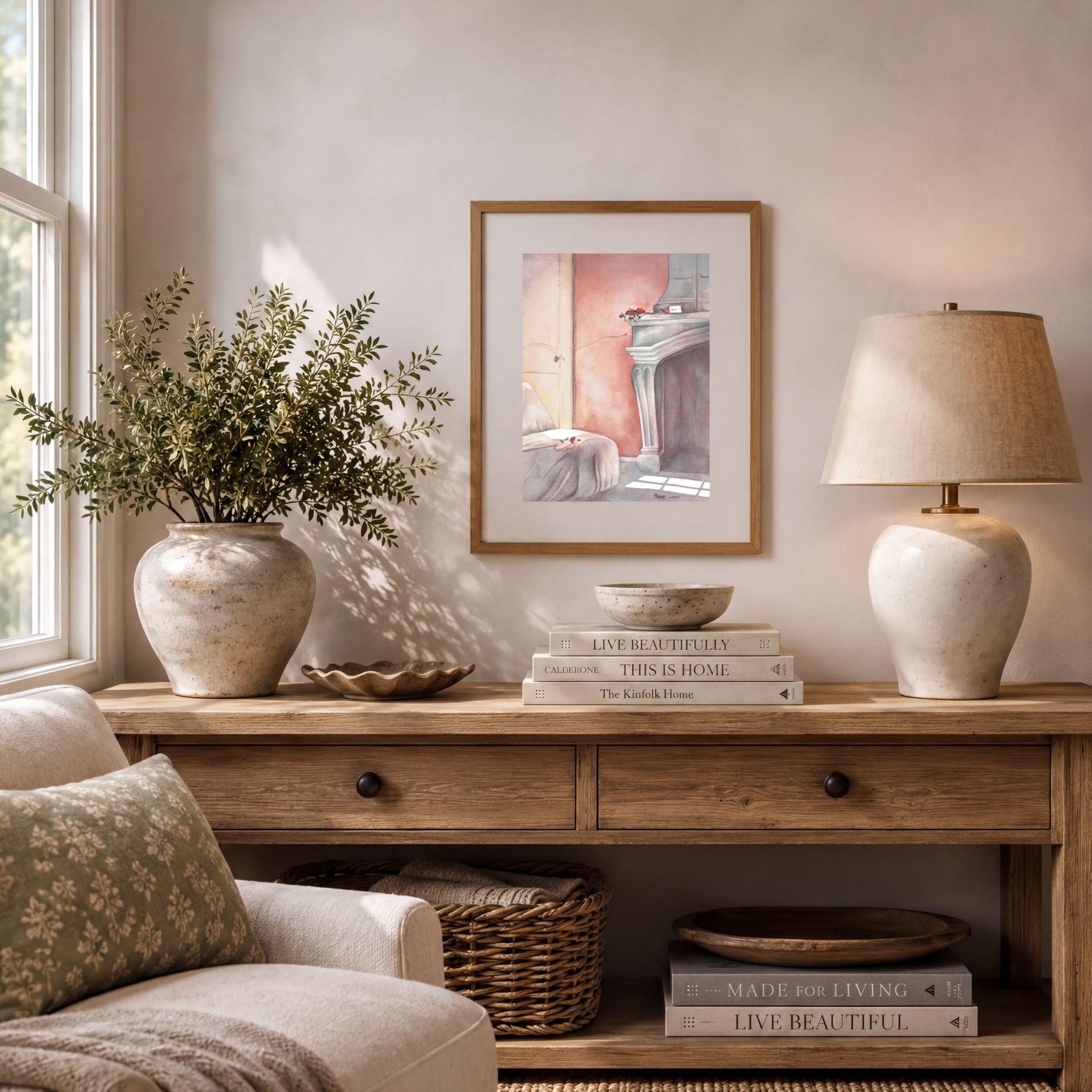 a cozy living room with a wooden console table, a lamp, a framed picture, and a plant. The table has a stack of books and a bowl on it. The room has a window that allows natural light to enter, and there is a comfortable couch in the background.