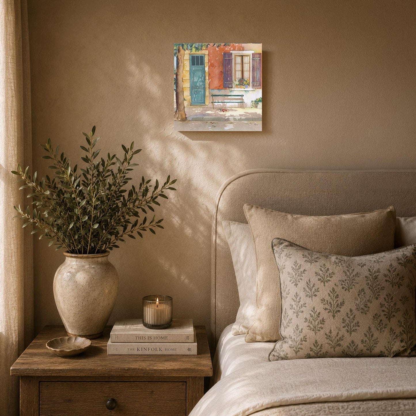 a cozy bedroom scene with a bed, a nightstand, and a painting of a house on the wall. The bed is adorned with patterned pillows and a vase of greenery, creating a warm and inviting atmosphere. The nightstand has a stack of books and a candle, adding a touch of elegance and relaxation to the space. The painting of the house adds a personal and artistic element to the room.