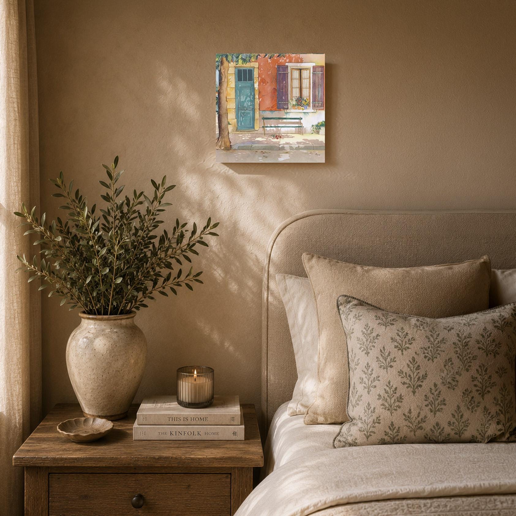 a cozy bedroom scene with a bed, a nightstand, and a painting of a house on the wall. The bed is adorned with patterned pillows and a vase of greenery, creating a warm and inviting atmosphere. The nightstand has a stack of books and a candle, adding a touch of elegance and relaxation to the space. The painting of the house adds a personal and artistic element to the room.