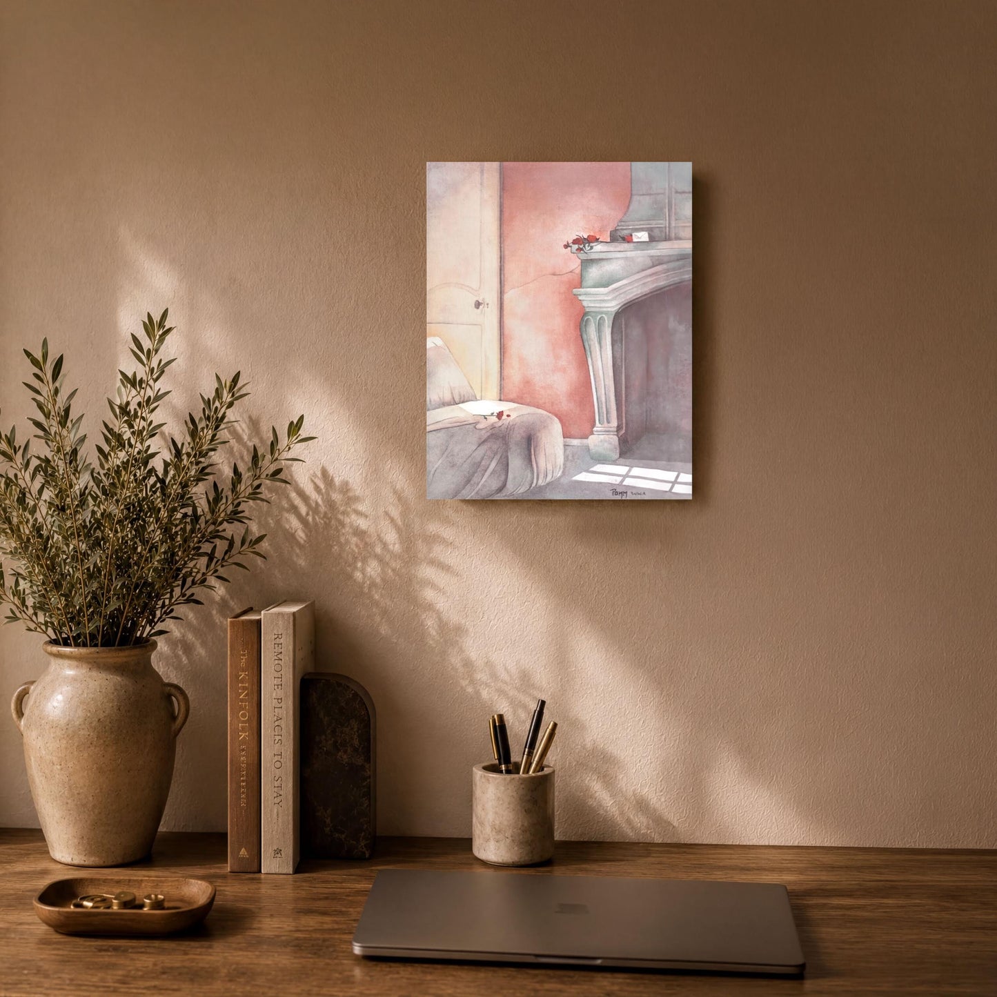 a wooden desk with a laptop, a vase with greenery, and a framed painting of a fireplace.