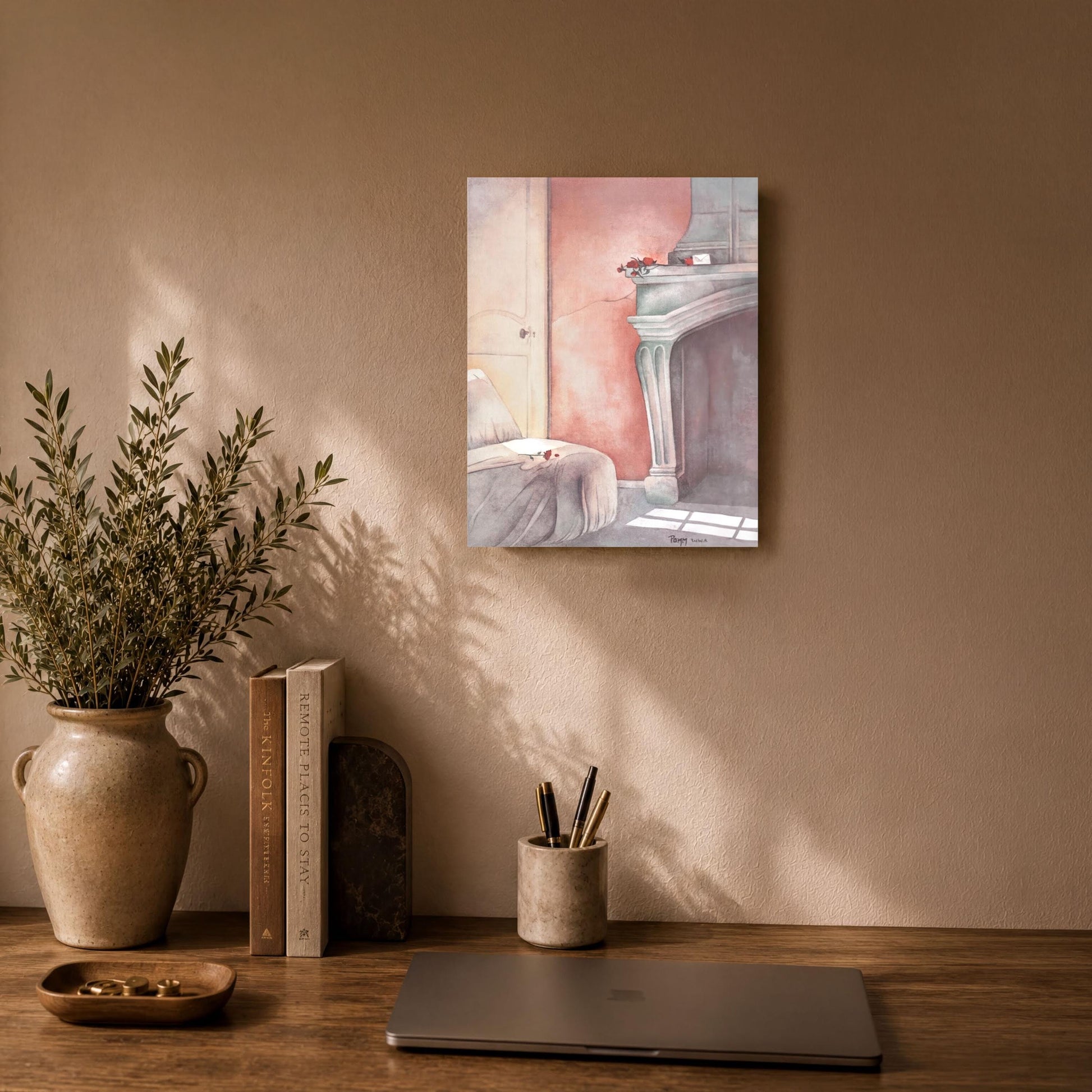 a wooden desk with a laptop, a vase with greenery, and a framed painting of a fireplace.
