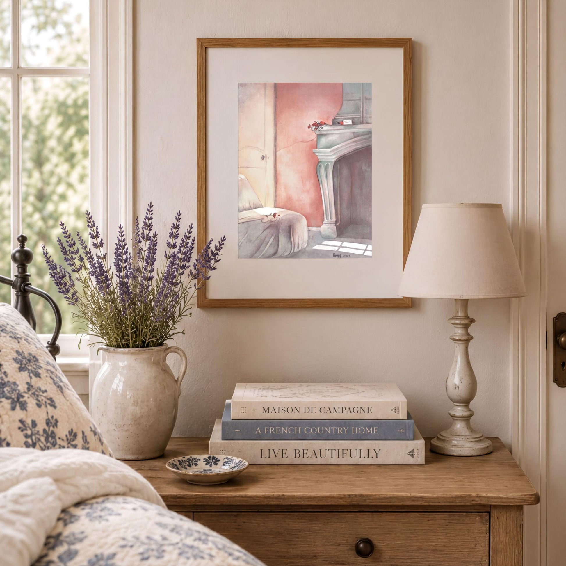 a cozy bedroom scene with a framed painting of a fireplace, a vase of lavender flowers, a stack of books, and a lamp on a wooden nightstand.