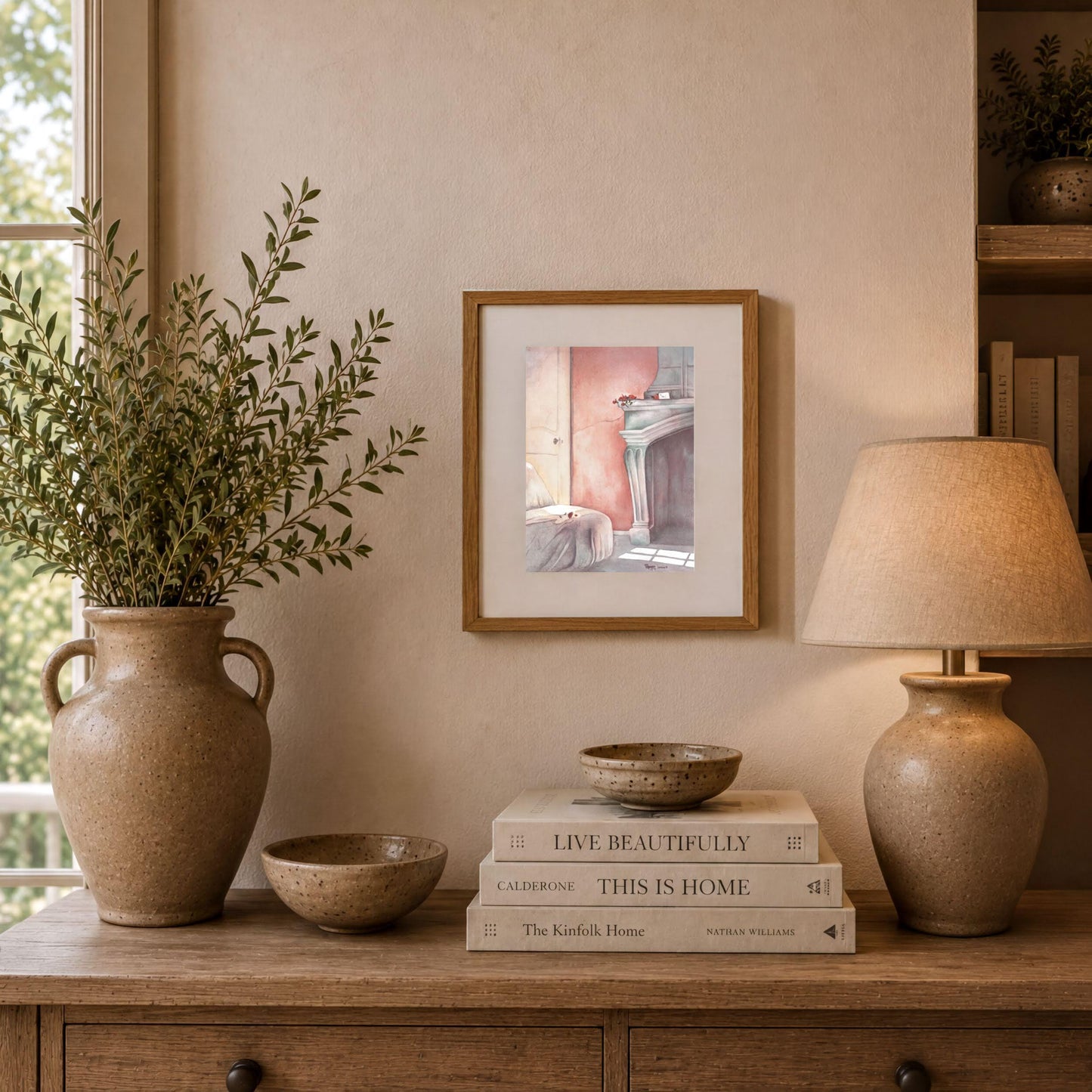 a wooden table with a vase of greenery, a stack of books, a lamp, and a framed picture on the wall.